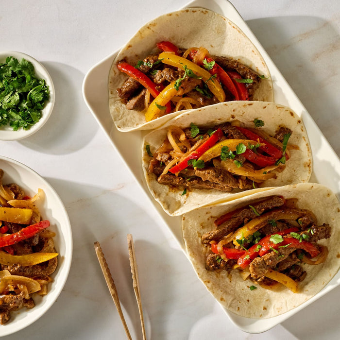 Three soft tacos filled with seasoned steak, peppers, onions, and cilantro, with a McCormick Fajita seasoning packet.