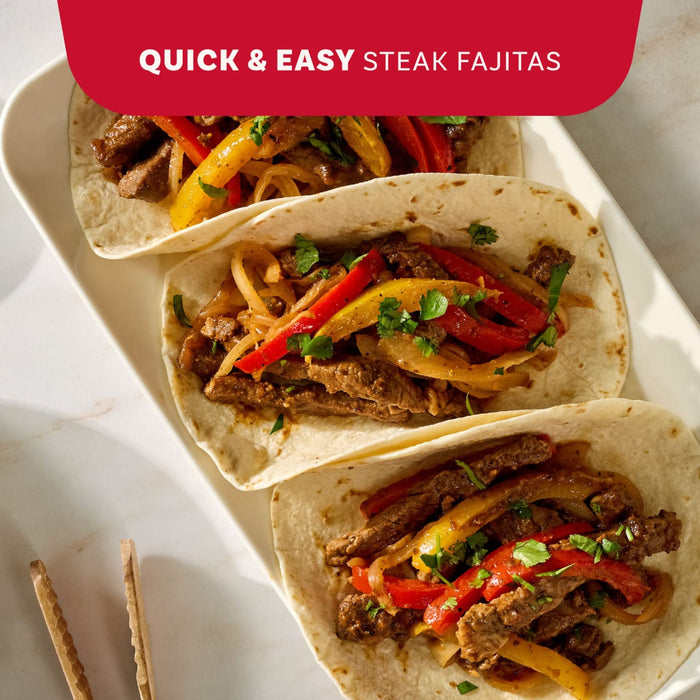 A white plate with a steak fajita on a tortilla with lime wedges on a red background.