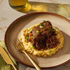 A plate of braised short ribs served over creamy polenta, garnished with green onions.