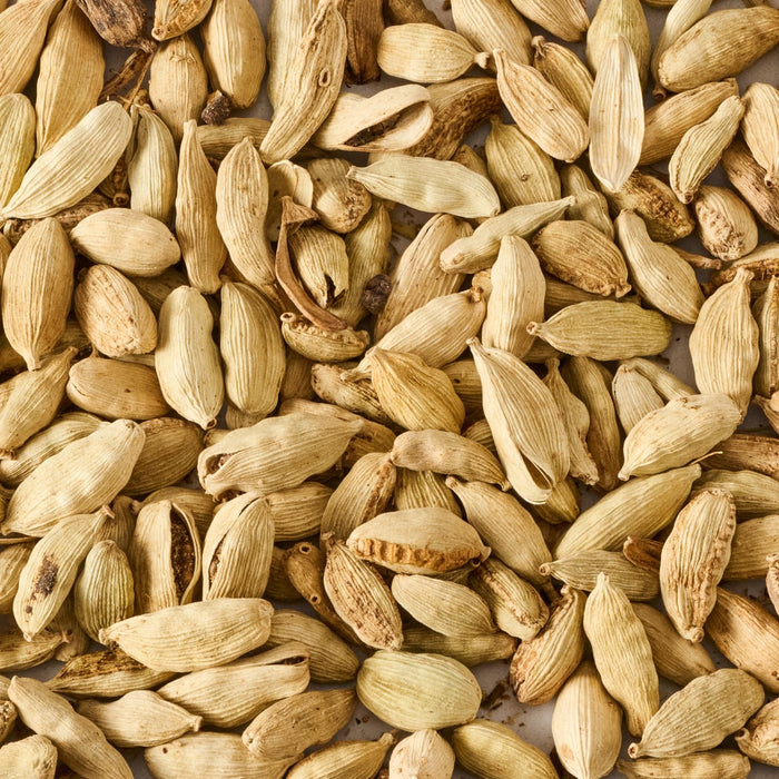 A close-up shows a pile of dried cardamom pods, highlighting their texture and color.