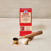 A box of McCormick Small Batch Pure Vanilla Extract sits next to measuring spoons with vanilla extract spilled on the surface.