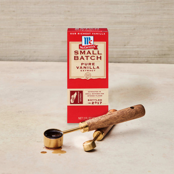 A box of McCormick Small Batch Pure Vanilla Extract sits next to measuring spoons with vanilla extract spilled on the surface.