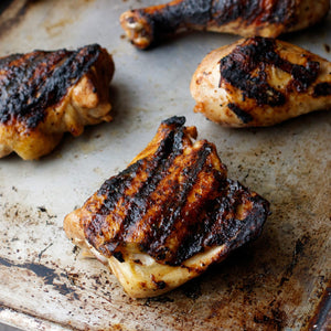 Grilled chicken pieces with dark grill marks are arranged on a baking sheet.