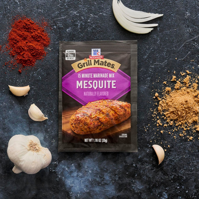 A packet of Grill Mates Mesquite Marinade Mix is displayed with garlic cloves and piles of red and brown spices.