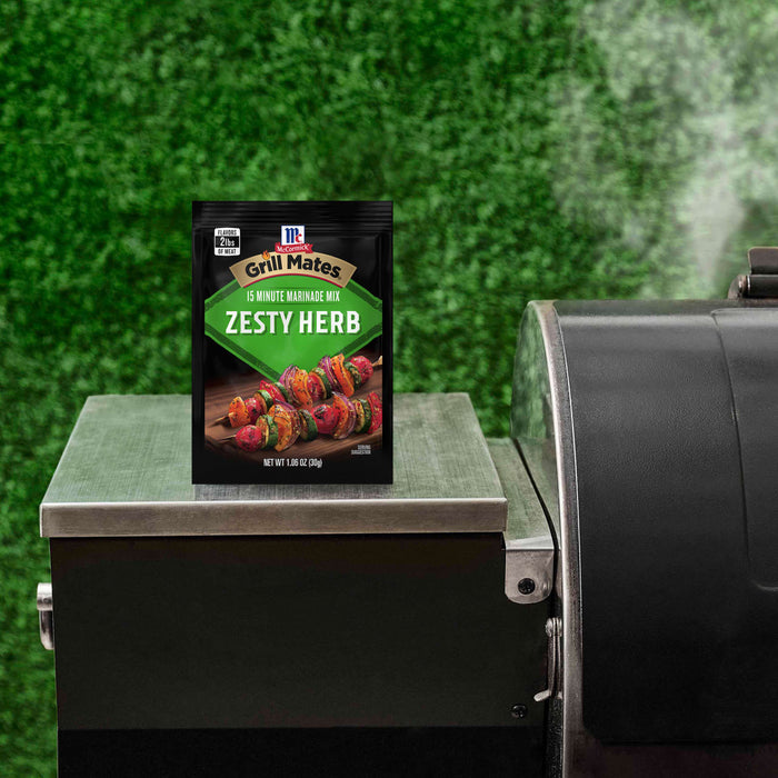 A packet of McCormick Grill Mates Zesty Herb Marinade Mix sits on a grill, suggesting its use for outdoor cooking.