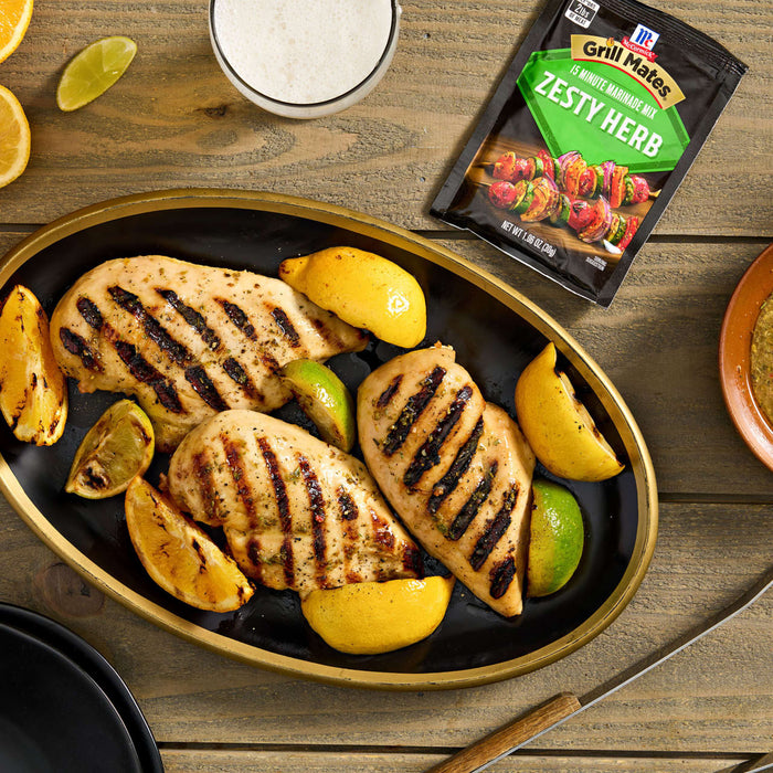 Grilled chicken breasts seasoned with McCormick Zesty Herb marinade mix are arranged on a platter with grilled lemon and lime wedges.