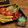 Grilled vegetables arranged on a black tray with a McCormick Zesty Herb marinade mix packet.