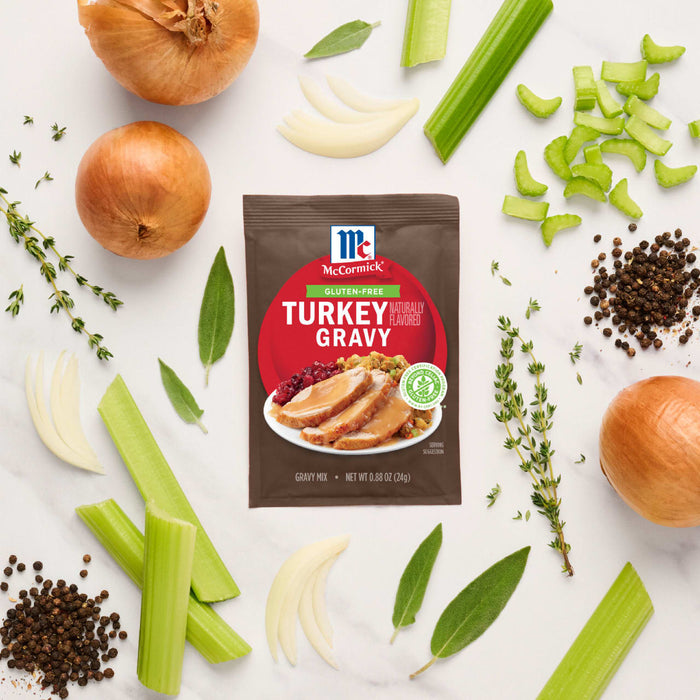 A packet of McCormick Turkey Gravy mix is surrounded by fresh ingredients like onions, celery, and herbs, suggesting a homemade gravy flavor.