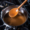 A wooden spoon is being used to stir a pot of gravy on a stovetop.