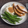 A plate of sliced turkey with gravy, mashed potatoes, and green beans.