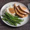 A plate of sliced turkey with gravy, mashed potatoes, and green beans.