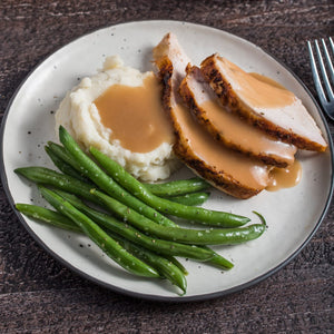 A plate of sliced turkey with gravy, mashed potatoes, and green beans.