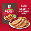 A packet of McCormick Gluten-Free Turkey Gravy mix is displayed next to a plate of turkey, cranberry sauce, and stuffing, highlighting the rich, savory flavor of the gravy.