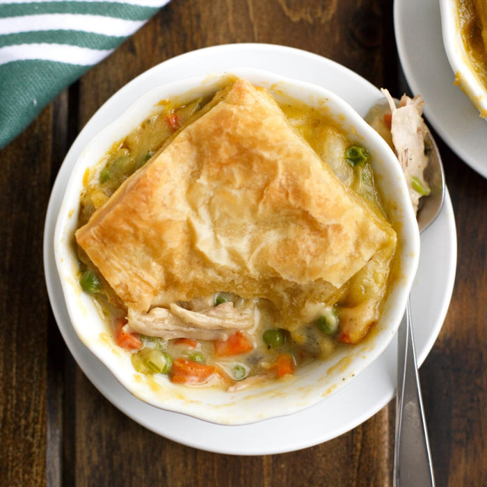 A delicious chicken pot pie with a golden, flaky crust sits in a white bowl on a wooden table.