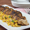 A grilled pork tenderloin is sliced and served on a white platter with a vibrant mango salsa.
