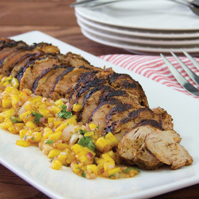 A grilled pork tenderloin is sliced and served on a white platter with a vibrant mango salsa.
