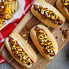 A wooden board displays three chili dogs topped with mustard and onions, accompanied by a side of waffle fries with melted cheese.