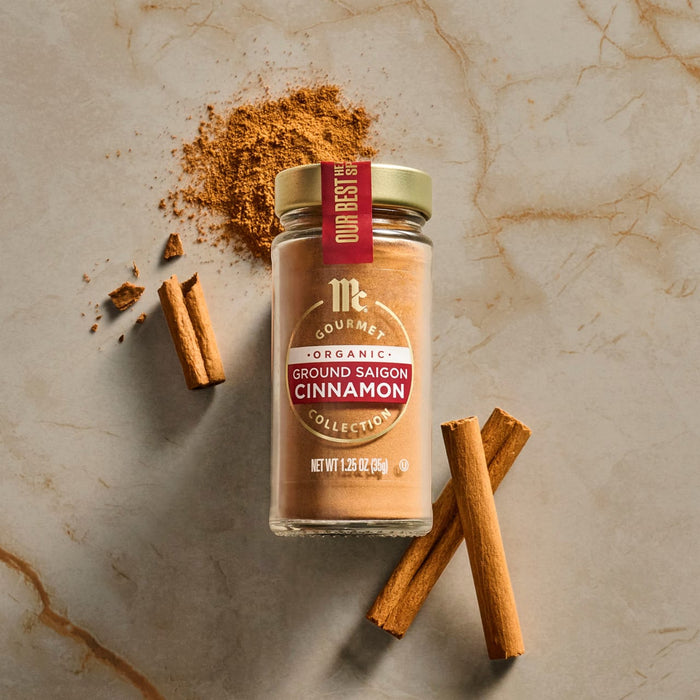 A jar of McCormick Gourmet Cinnamon is displayed with cinnamon sticks and powder on a marble surface.