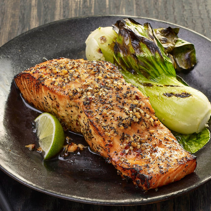 A plate of grilled salmon with bok choy and a lime wedge.