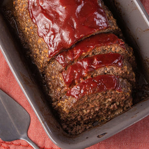A close-up of a meatloaf sliced and covered in a red sauce in a baking dish.