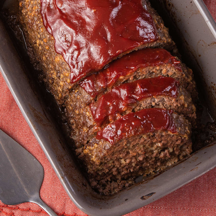 A close-up of a meatloaf sliced and covered in a red sauce in a baking dish.