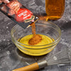 A packet of Maggi Fix für Chili Cheese Burger seasoning is being poured into a bowl with a yellow liquid, likely for preparing a sauce or marinade.