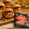 A close-up of pulled chicken sliders on a wooden board next to a package of Grill Mates Applewood Seasoning Mix.