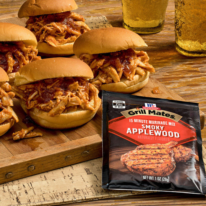 A close-up of pulled chicken sliders on a wooden board next to a package of Grill Mates Applewood Seasoning Mix.