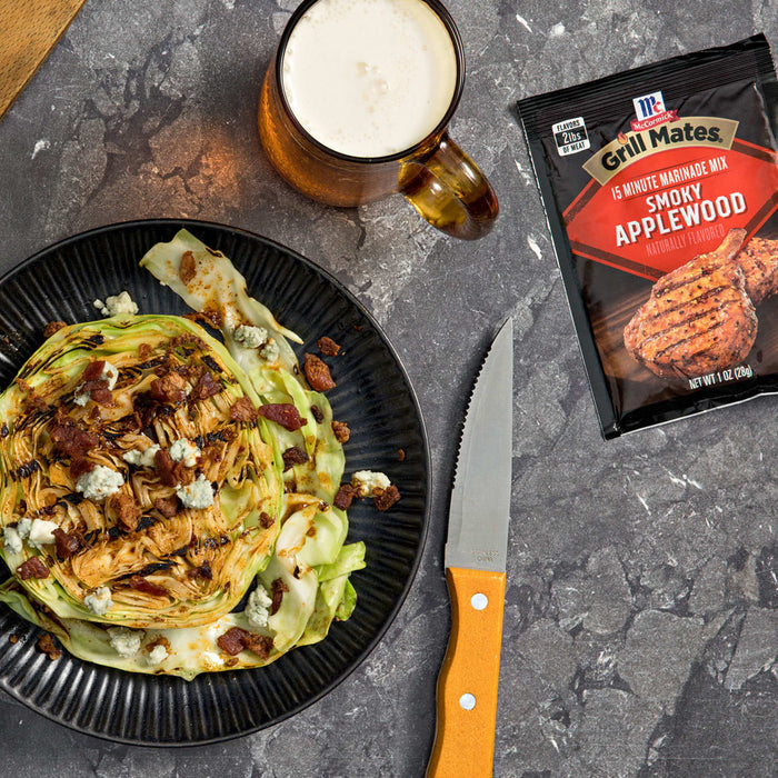 A plate of grilled lettuce wedge salad with blue cheese crumbles and bacon bits, alongside a package of McCormick Grill Mates Montreal Chicken seasoning and a mug of beer.