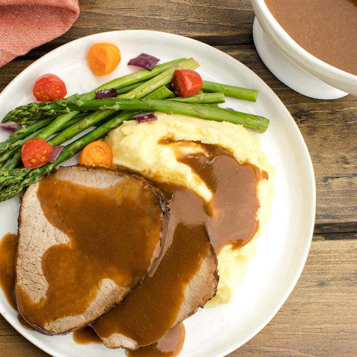 A plate of roast beef with mashed potatoes asparagus and gravy.