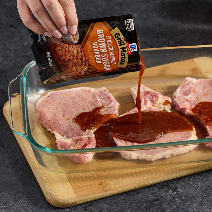 A hand pours a packet of McCormick Brown Sugar Marinade onto pork chops in a glass baking dish.