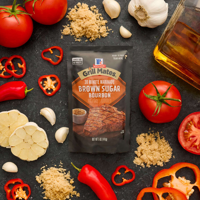 A packet of McCormick Grill Mates Brown Sugar Bourbon seasoning is surrounded by fresh ingredients like tomatoes, garlic, and peppers.