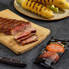 A grilled steak sliced on a wooden board, served with corn on the cob and McCormick Brown Sugar Bourbon seasoning.
