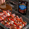 A hand pours marinade from a glass measuring cup onto skewers of meat and vegetables, with a Club House Montreal Steak spice packet in the background.