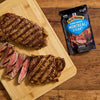 Grilled steak seasoned with McCormick Montreal Steak Seasoning is displayed on a wooden cutting board.