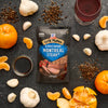 A package of Grill Mates Montreal Steak seasoning is surrounded by ingredients like garlic, peppercorns, oranges, and red wine, suggesting a flavorful steak preparation.