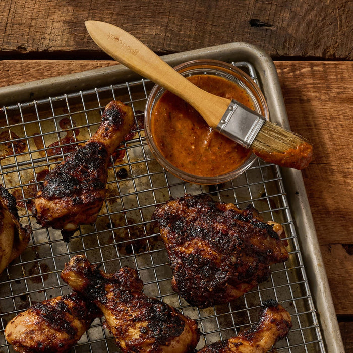 A close-up of grilled chicken pieces on a wire rack with a bowl of sauce and a brush, suggesting a delicious and flavorful meal.