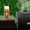 A bottle of Kosmos Q Dirty Bird BBQ Rub sits next to a smoker, suggesting its use in grilling.