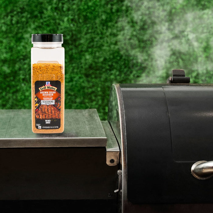 A bottle of Kosmos Q Dirty Bird BBQ Rub sits next to a smoker, suggesting its use in grilling.