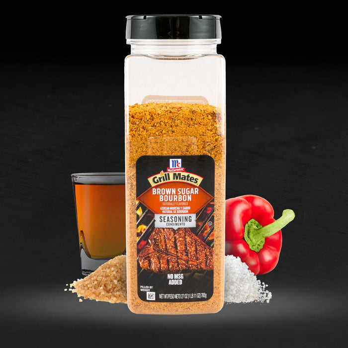 A bottle of McCormick Grill Mates Brown Sugar Bourbon seasoning is displayed with brown sugar, salt, a red pepper, and a glass of bourbon.