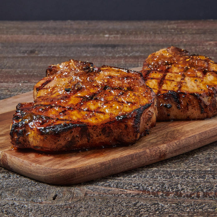 Two grilled pork chops with visible grill marks sit on a wooden cutting board.