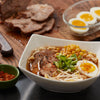 A bowl of ramen with pork corn bean sprouts green onions and a soft boiled egg.