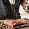 A chef seasons a rack of ribs with spices, preparing it for cooking.