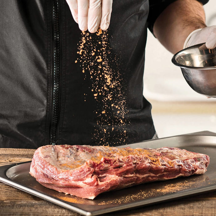 A chef seasons a rack of ribs with spices, preparing it for cooking.