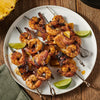 A plate of grilled shrimp skewers with pineapple and bacon.