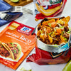 A bag of McCormick Original Taco seasoning next to a bag of tortilla chips filled with ground beef lettuce tomatoes and cheese.