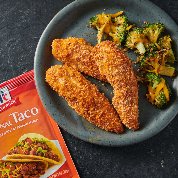 A plate of breaded chicken tenders and broccoli with cheese sauce next to a McCormick Taco Seasoning packet.