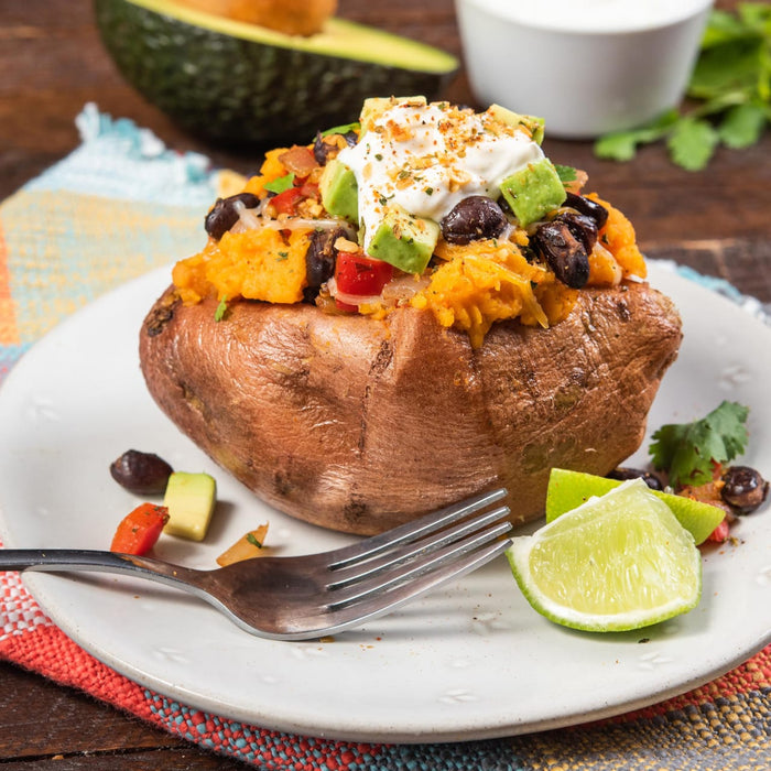 A baked sweet potato topped with black beans avocado sour cream and spices.