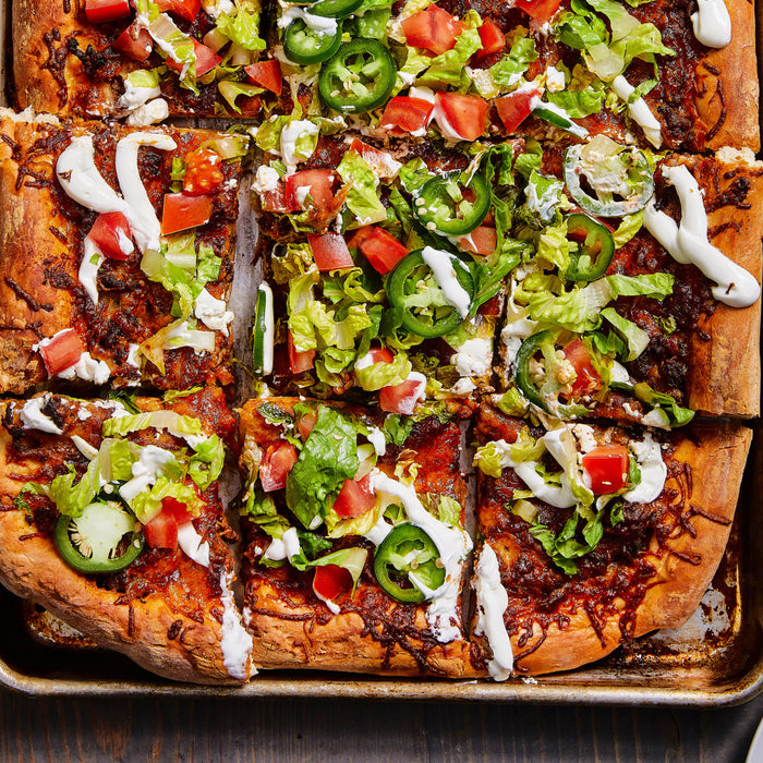 A close-up of a sheet pan pizza with toppings of lettuce tomatoes jalapenos and sour cream.