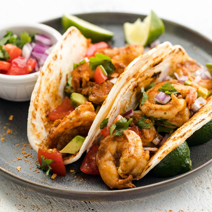 Two shrimp tacos with avocado tomato onion and cilantro on a gray plate.